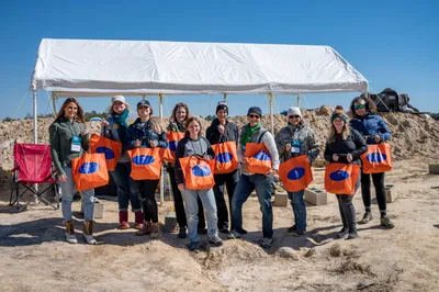 Teachers at the Montbrook fossil site holding orange SEFS tote bags after a professional development dig experience